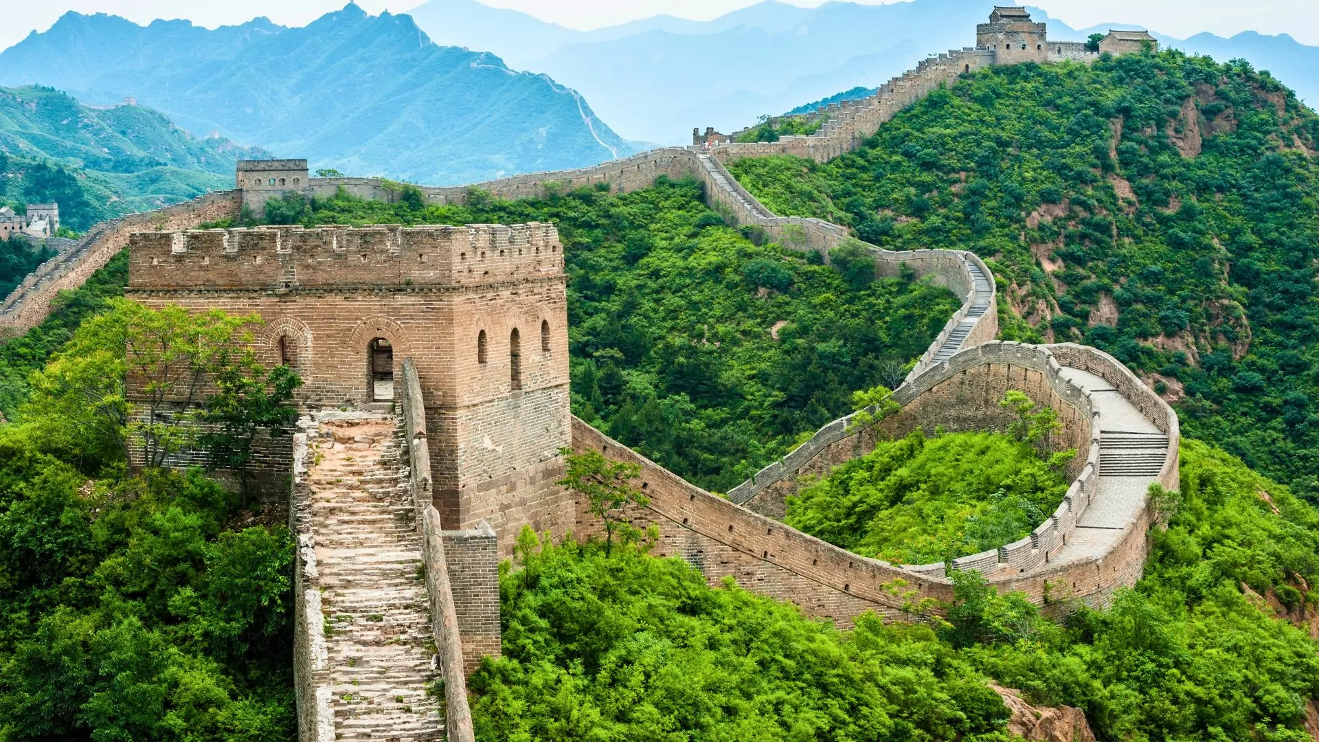 The Great Wall of China winds long forested green hilltops
