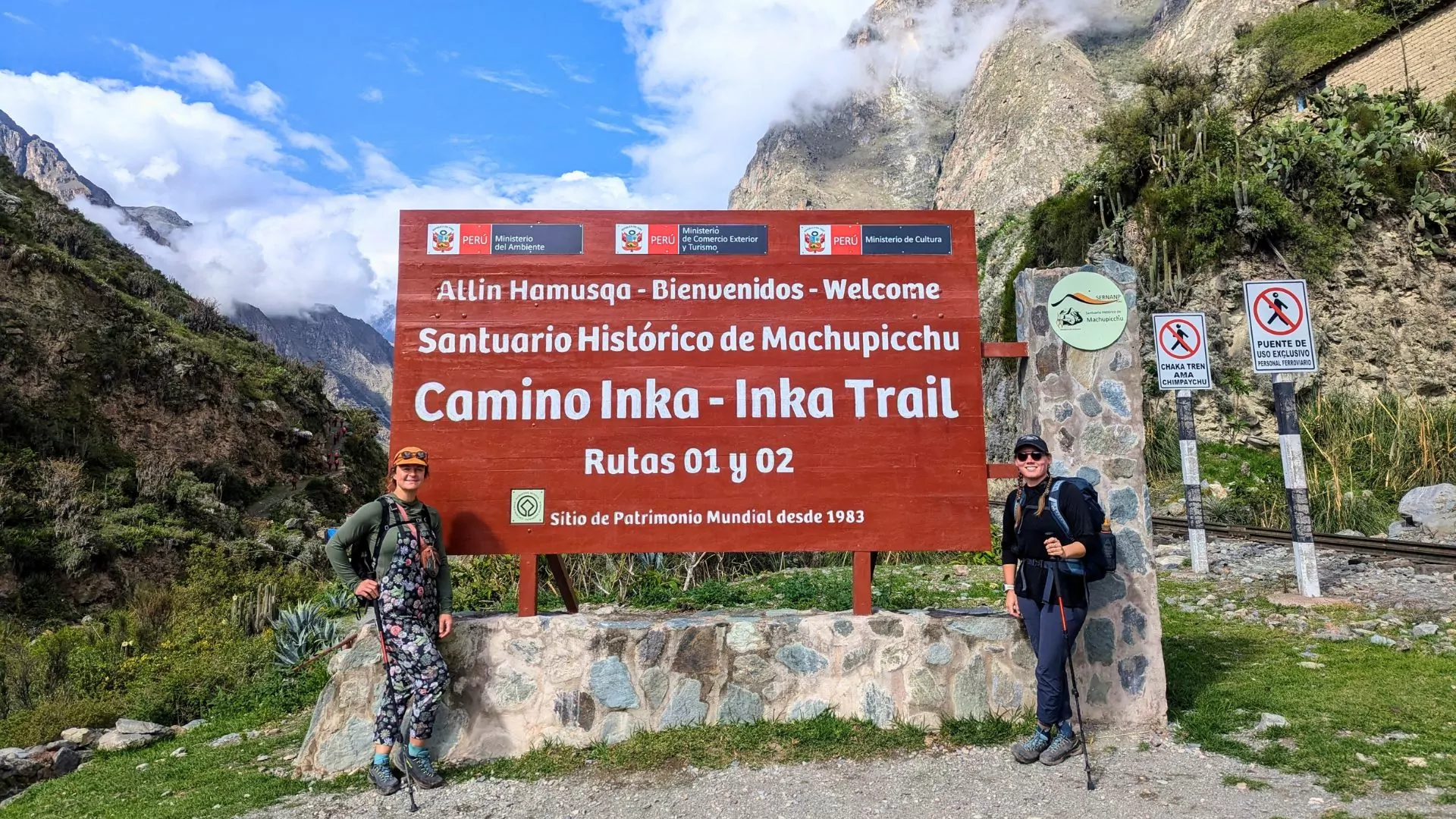 Two women stand in front of a sign at the beginning of the Inca Trail in Peru