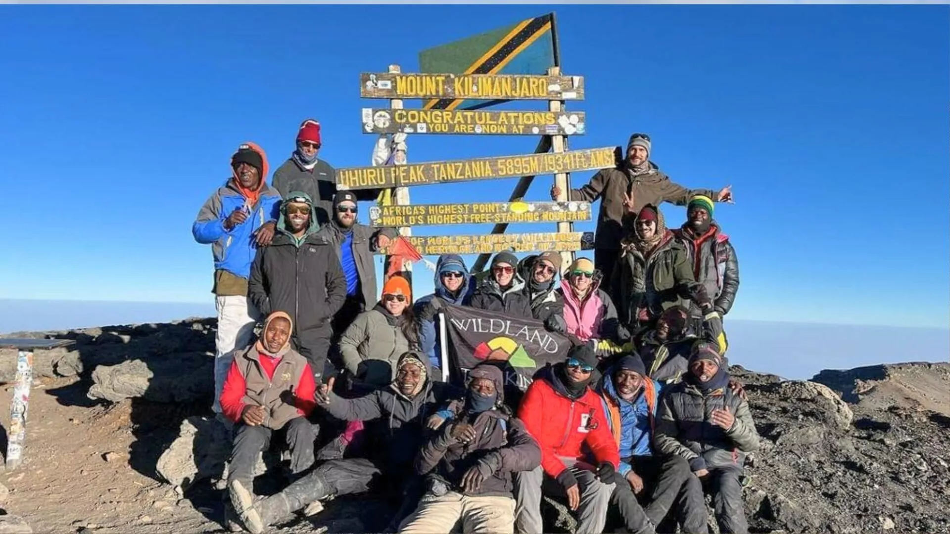 Several hikers pose in front of the Kilimanjaro summit sign