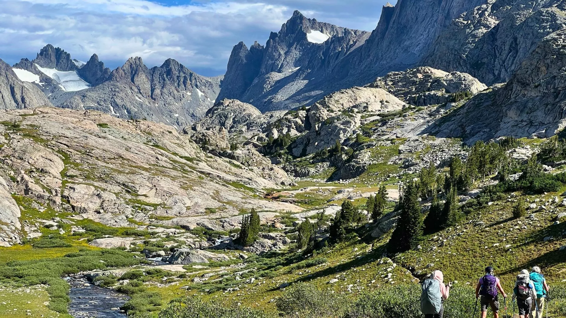 Four hikers walk through a mountainous alpine landscape in wyoming's wind river range