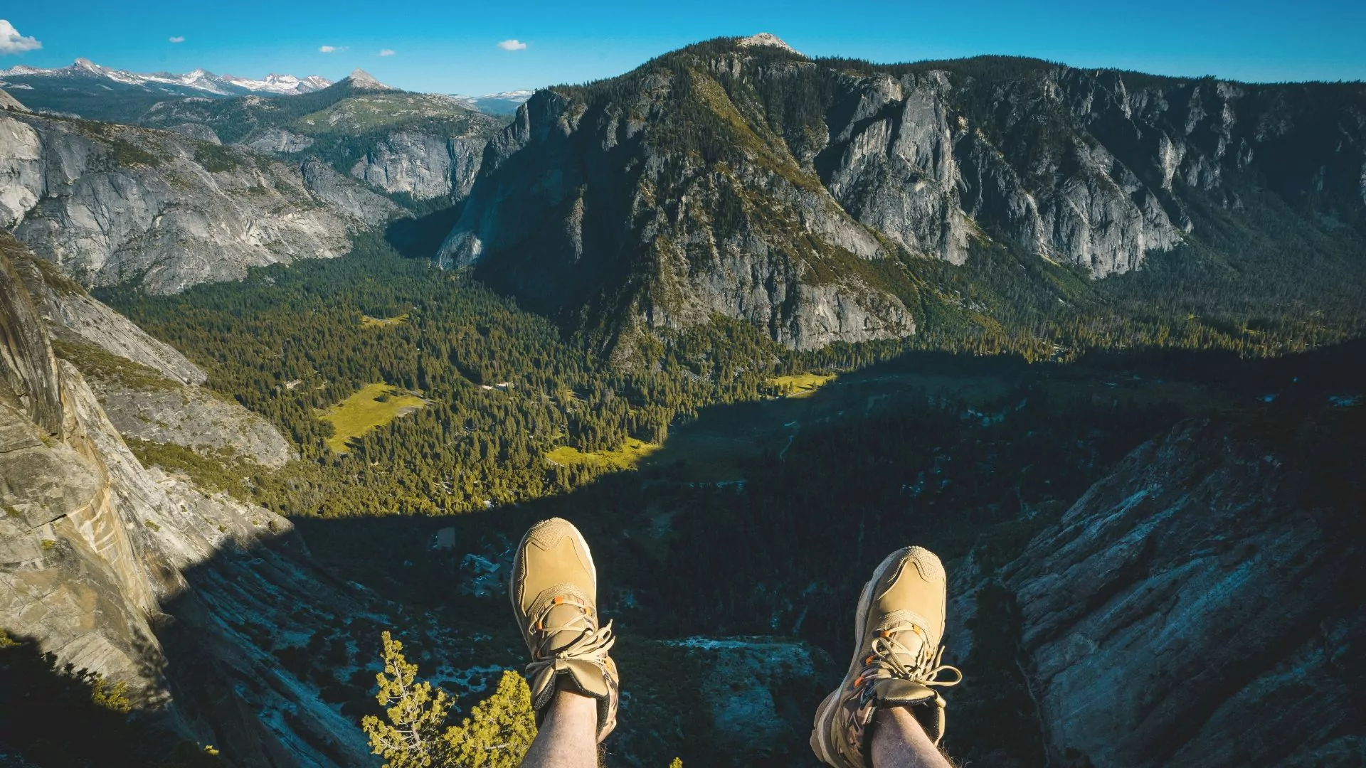 A pair of feet dangle over the edge of a precipitous drop off with a beautiful view of yosemite below