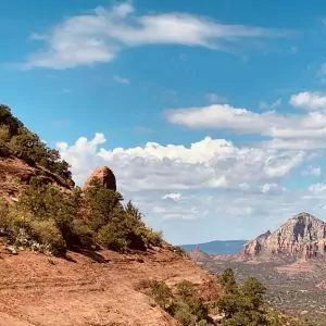 Light blue skies, puffy clouds, sandstone rock formations and desert flora